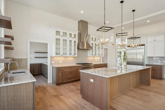 kitchen with light wood-type flooring, sink, wall chimney range hood, high quality appliances, and white cabinetry