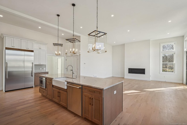 kitchen featuring stainless steel appliances, a kitchen island with sink, sink, pendant lighting, and white cabinets