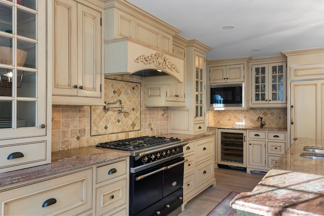 kitchen featuring black appliances, cream cabinets, light stone counters, and wine cooler