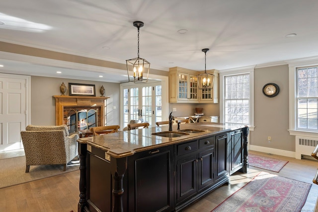 kitchen with sink, decorative light fixtures, light hardwood / wood-style floors, an island with sink, and radiator heating unit