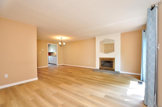 29 Early Dawn Cir Unit 29, Windsor, CT 06095 - unfurnished living room featuring a chandelier, a glass covered fireplace, and light wood-style floors