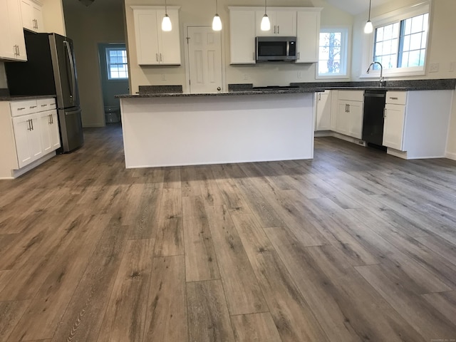 kitchen with appliances with stainless steel finishes, white cabinetry, hanging light fixtures, and a kitchen island