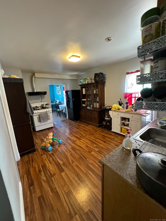 kitchen featuring hardwood / wood-style floors, black refrigerator, white cabinets, and white gas stove