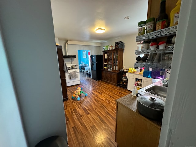 kitchen with white cabinets, sink, black refrigerator, white gas range, and wood-type flooring