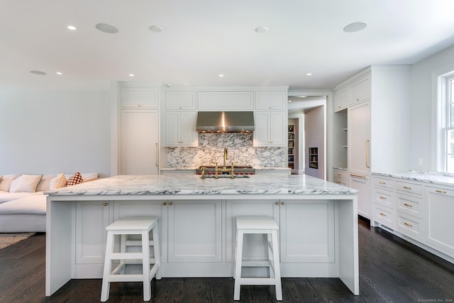 kitchen featuring light stone countertops, a breakfast bar, wall chimney range hood, and a spacious island