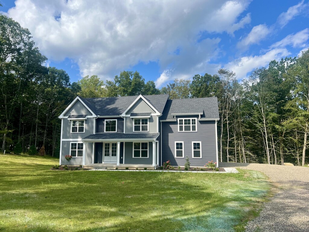 view of front of house featuring gravel driveway, a shingled roof, a porch, board and batten siding, and a front lawn