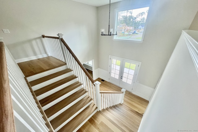 staircase featuring a high ceiling, hardwood / wood-style floors, a chandelier, and french doors