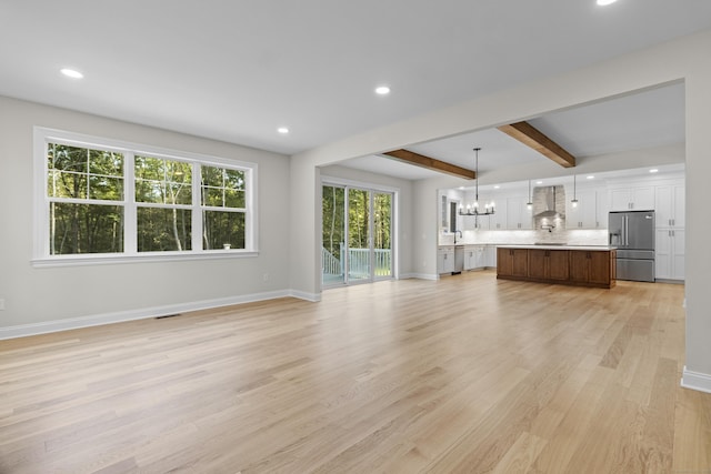 unfurnished living room with light wood finished floors, recessed lighting, an inviting chandelier, beamed ceiling, and baseboards