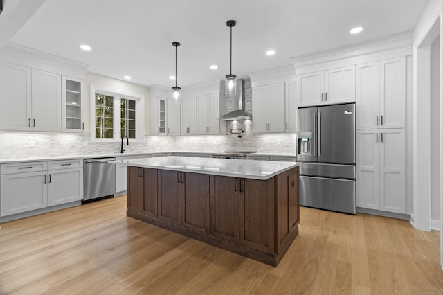 kitchen featuring appliances with stainless steel finishes, light countertops, light wood-type flooring, wall chimney range hood, and white cabinetry