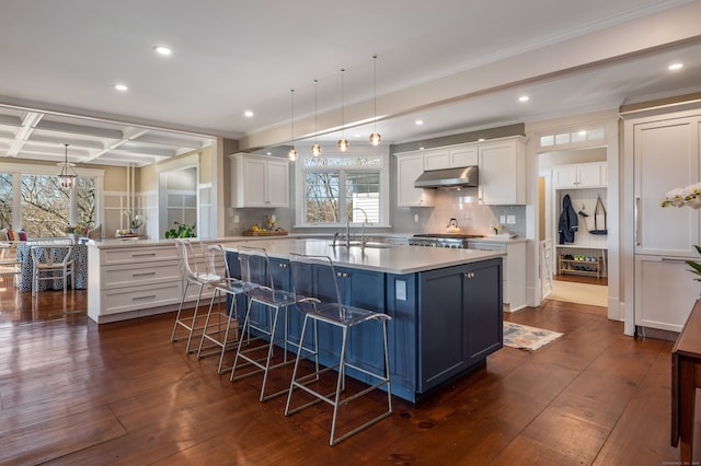 kitchen with pendant lighting, an island with sink, coffered ceiling, dark hardwood / wood-style floors, and backsplash