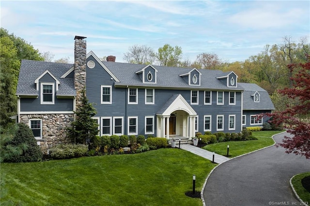 view of front of property featuring a front yard, a chimney, stone siding, and a shingled roof