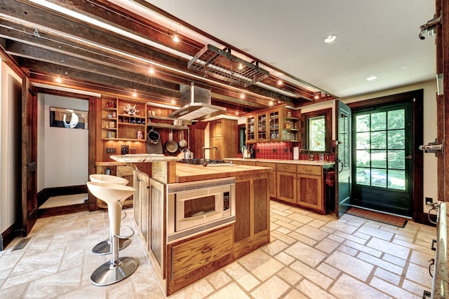 kitchen featuring stainless steel appliances, a kitchen breakfast bar, range hood, and an island with sink