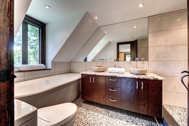 bathroom with tile walls, toilet, a tub to relax in, and vanity