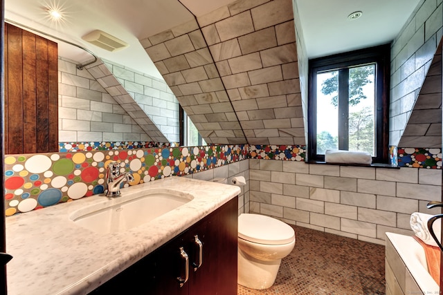 bathroom featuring toilet, lofted ceiling, a bathing tub, tile walls, and vanity