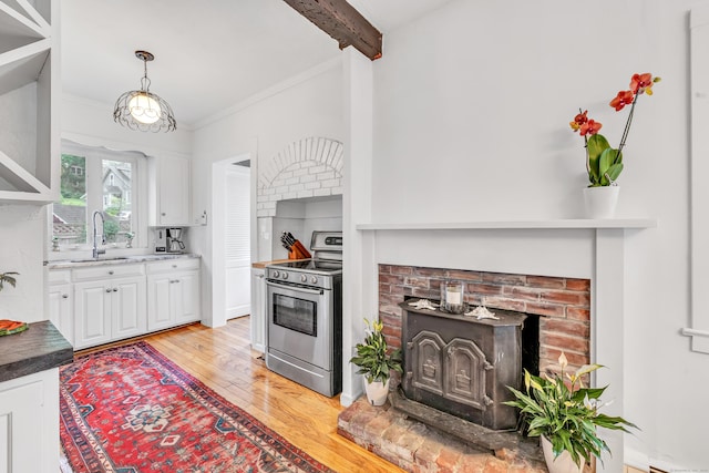 kitchen featuring white cabinetry, a wood stove, stainless steel electric range oven, and sink