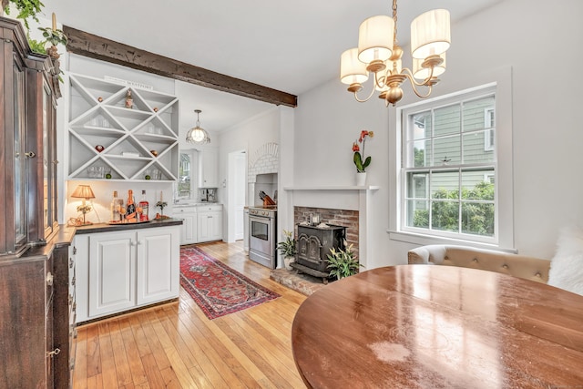 interior space with beam ceiling, light hardwood / wood-style floors, a wood stove, and a notable chandelier