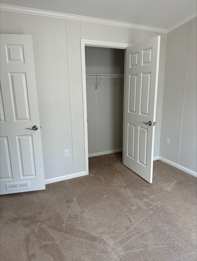 unfurnished bedroom with a closet, carpet flooring, and crown molding