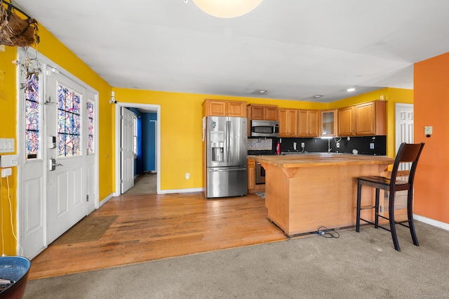 kitchen featuring light hardwood / wood-style floors, a kitchen breakfast bar, appliances with stainless steel finishes, kitchen peninsula, and tasteful backsplash