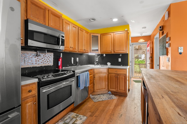 kitchen with light hardwood / wood-style floors, hanging light fixtures, stainless steel appliances, sink, and tasteful backsplash