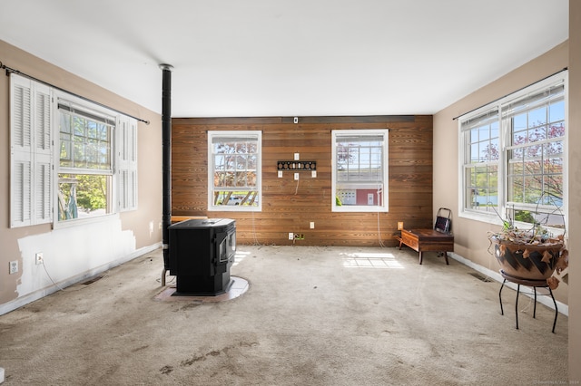 living area featuring carpet flooring, a wood stove, and a healthy amount of sunlight