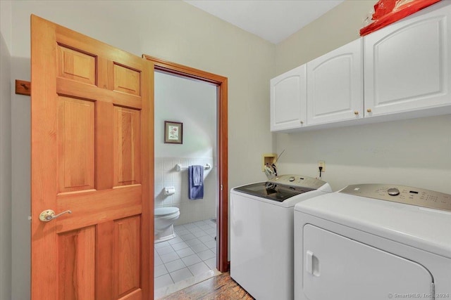 laundry room featuring cabinets, light tile patterned floors, washing machine and dryer, and tile walls