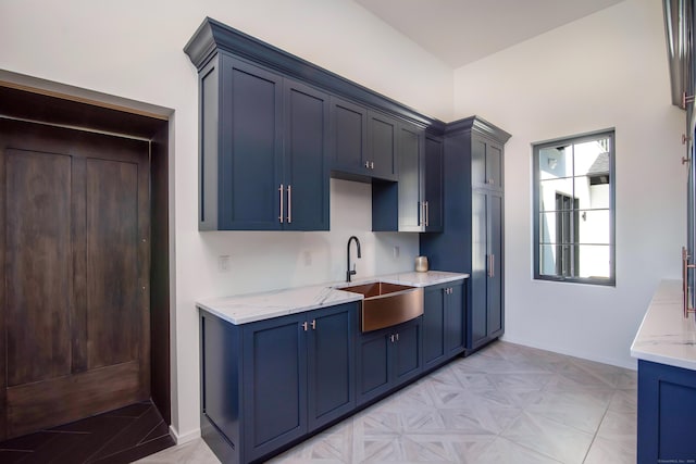 kitchen featuring light stone counters, sink, and blue cabinetry