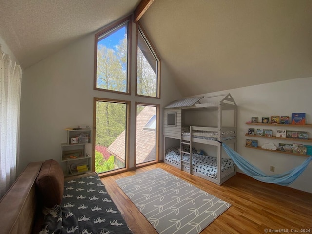 bedroom featuring beamed ceiling, hardwood / wood-style flooring, high vaulted ceiling, and a textured ceiling