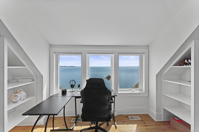 home office with plenty of natural light, light hardwood / wood-style floors, and a water view