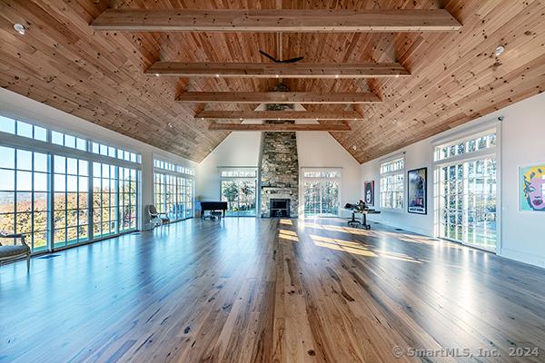 workout area with wood-type flooring, wooden ceiling, high vaulted ceiling, and a stone fireplace