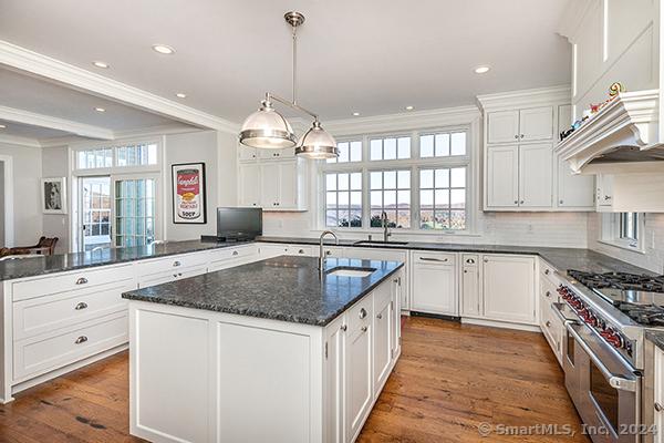 kitchen featuring a healthy amount of sunlight, high end stainless steel range, dark wood-type flooring, and an island with sink