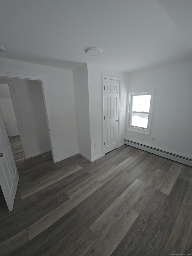 unfurnished bedroom with baseboard heating and dark hardwood / wood-style floors