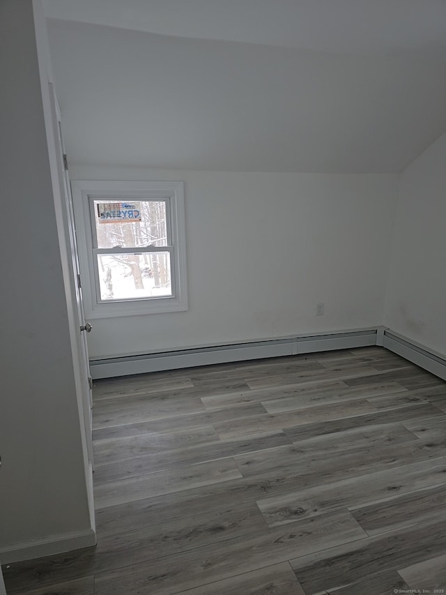 unfurnished room featuring baseboard heating, vaulted ceiling, and wood-type flooring