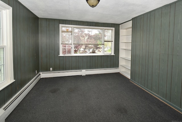 unfurnished room featuring dark colored carpet, baseboard heating, wood walls, and a textured ceiling