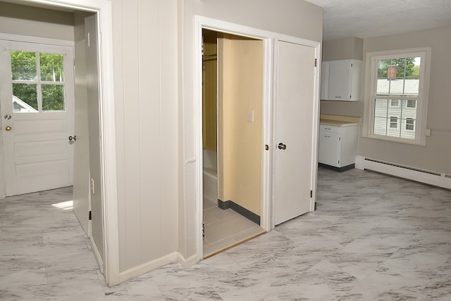 hallway with a baseboard radiator, a textured ceiling, and light tile flooring