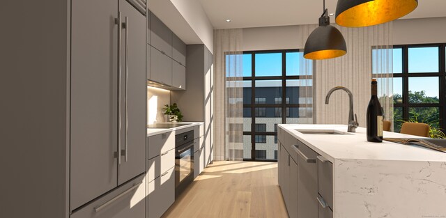 kitchen featuring a kitchen island with sink, black appliances, sink, decorative light fixtures, and gray cabinets