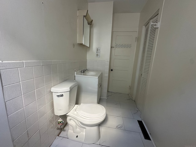 bathroom featuring toilet, vanity, tile walls, and tile patterned flooring