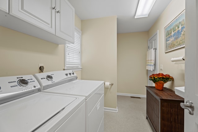 laundry area featuring washer and clothes dryer, light colored carpet, and cabinets