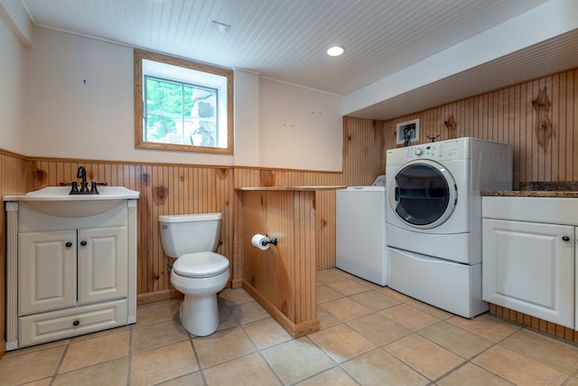 laundry area with wood walls, sink, washer and clothes dryer, and light tile floors