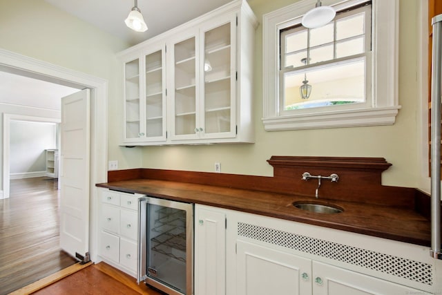 bar with wine cooler, white cabinets, decorative light fixtures, and sink