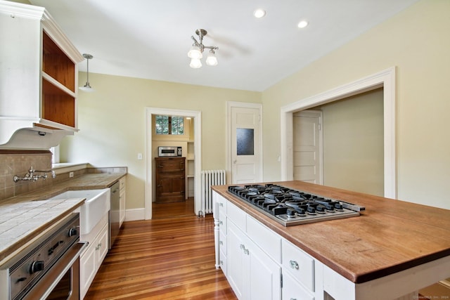 kitchen featuring appliances with stainless steel finishes, radiator heating unit, white cabinetry, and pendant lighting