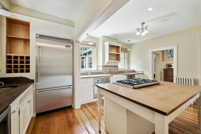 kitchen with white cabinets, radiator heating unit, stainless steel appliances, hanging light fixtures, and a breakfast bar area