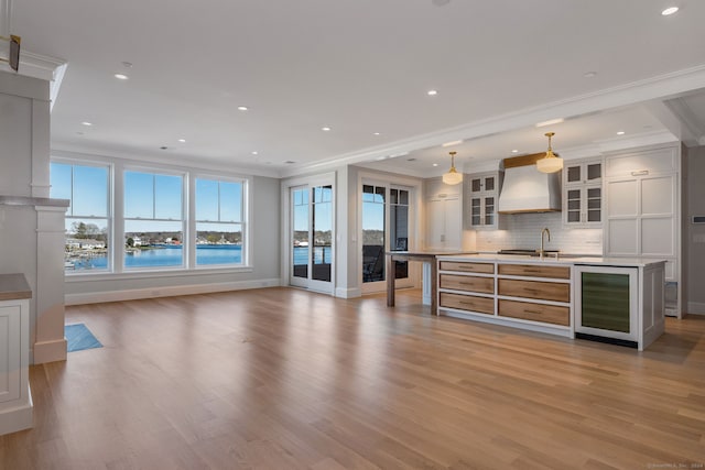 unfurnished living room with wine cooler, light hardwood / wood-style floors, a water view, sink, and ornamental molding