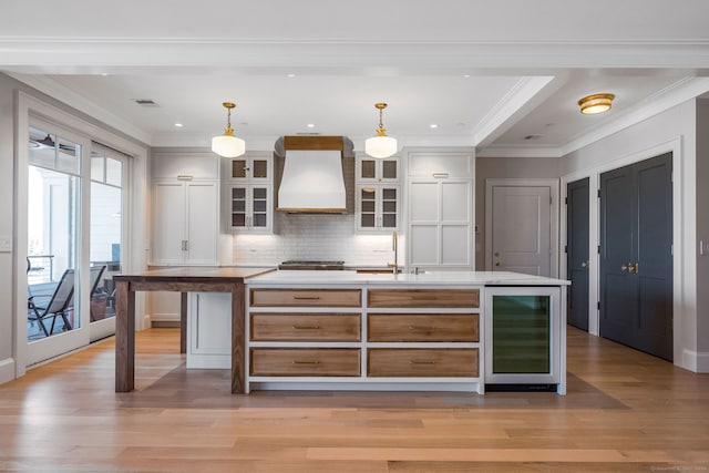 kitchen featuring decorative light fixtures, a center island with sink, custom exhaust hood, and light wood-type flooring