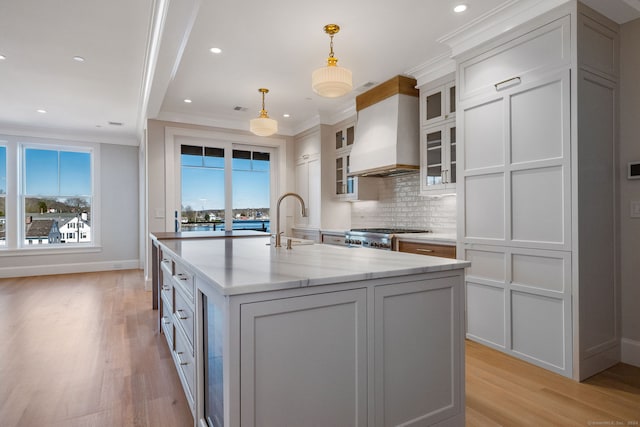 kitchen featuring decorative light fixtures, backsplash, custom exhaust hood, ornamental molding, and light wood-type flooring