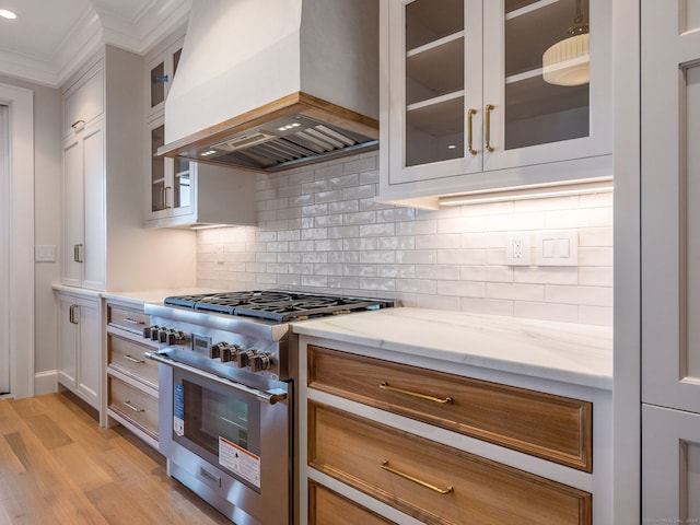 kitchen with light hardwood / wood-style flooring, stainless steel stove, premium range hood, light stone counters, and backsplash