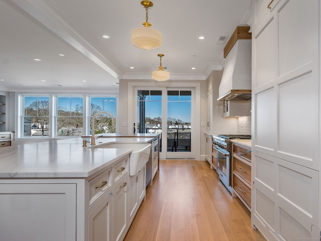 kitchen featuring light hardwood / wood-style floors, an island with sink, pendant lighting, double oven range, and custom exhaust hood