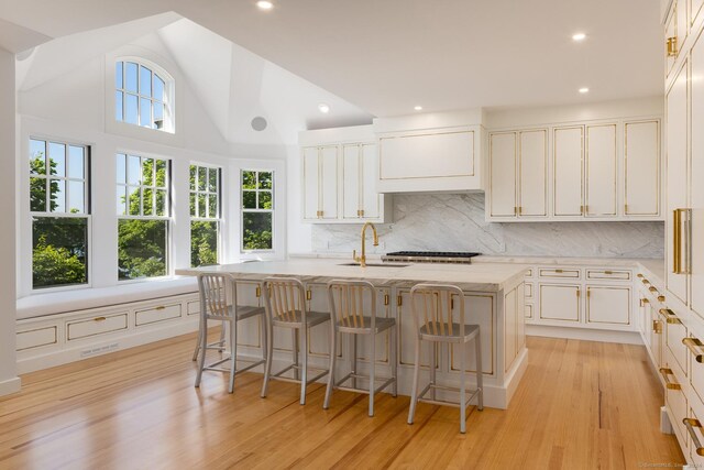 kitchen with a kitchen breakfast bar, light hardwood / wood-style floors, a kitchen island with sink, and tasteful backsplash