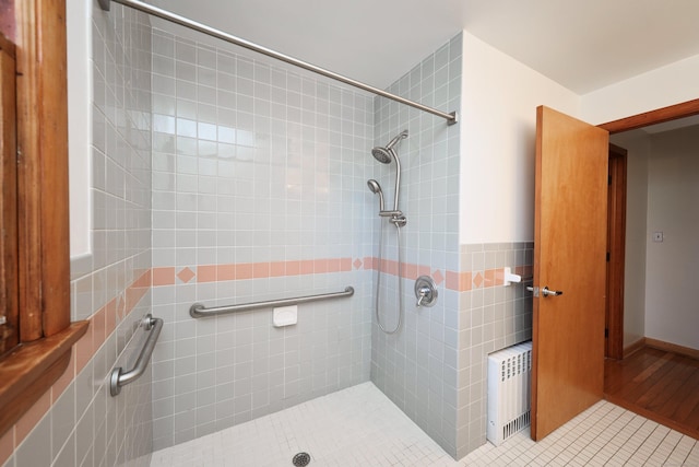 bathroom featuring tile patterned floors, a tile shower, tile walls, and radiator