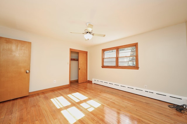 unfurnished bedroom with hardwood / wood-style floors, a closet, baseboard heating, and ceiling fan