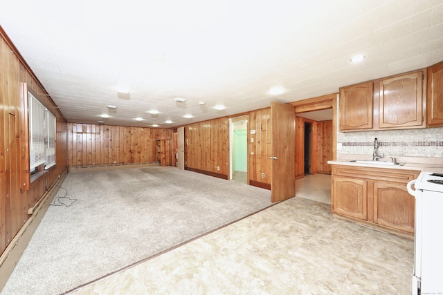 interior space featuring electric range, sink, wooden walls, a baseboard heating unit, and light carpet